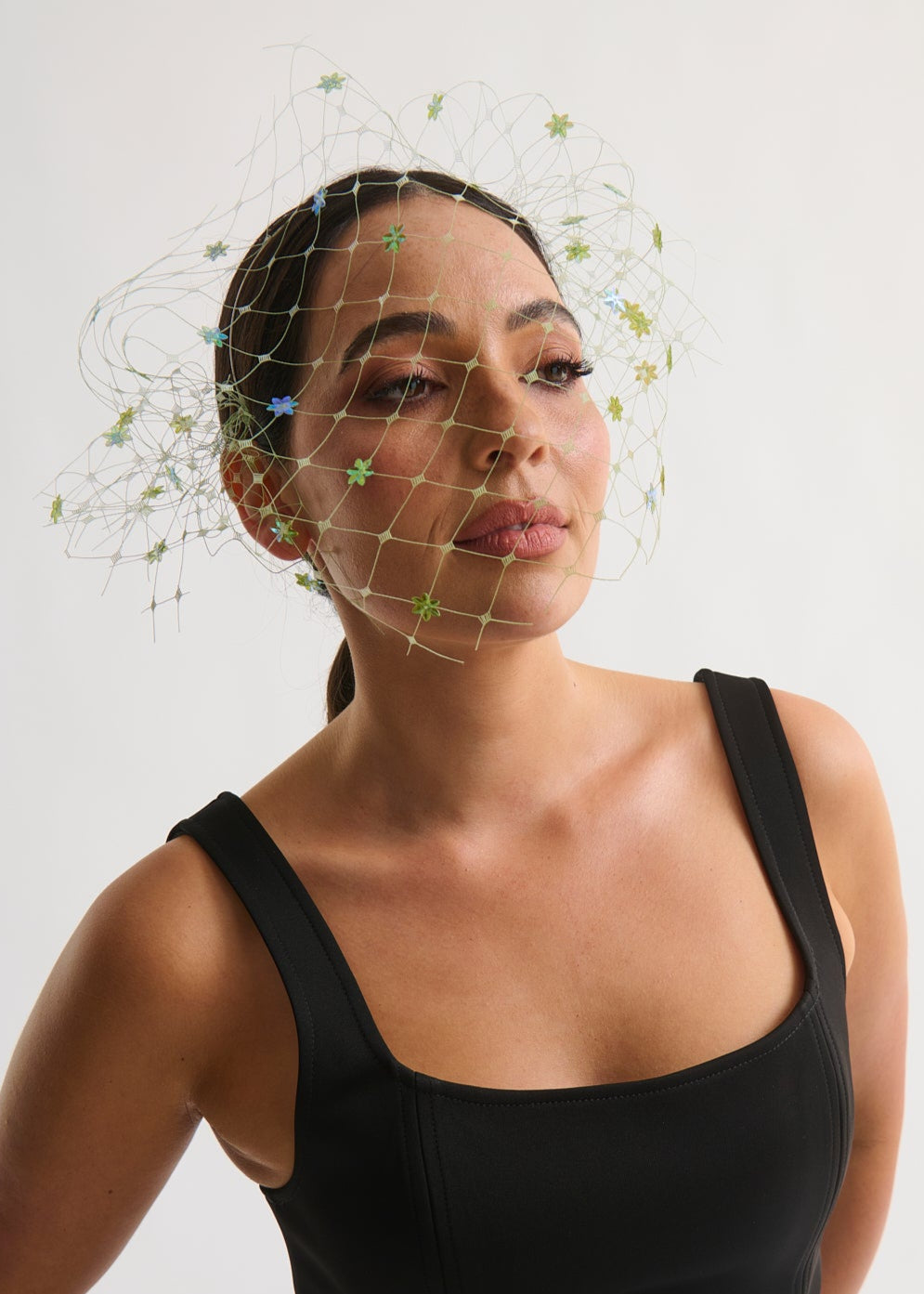 Woman wearing a black dress with a decorative headpiece against a plain background