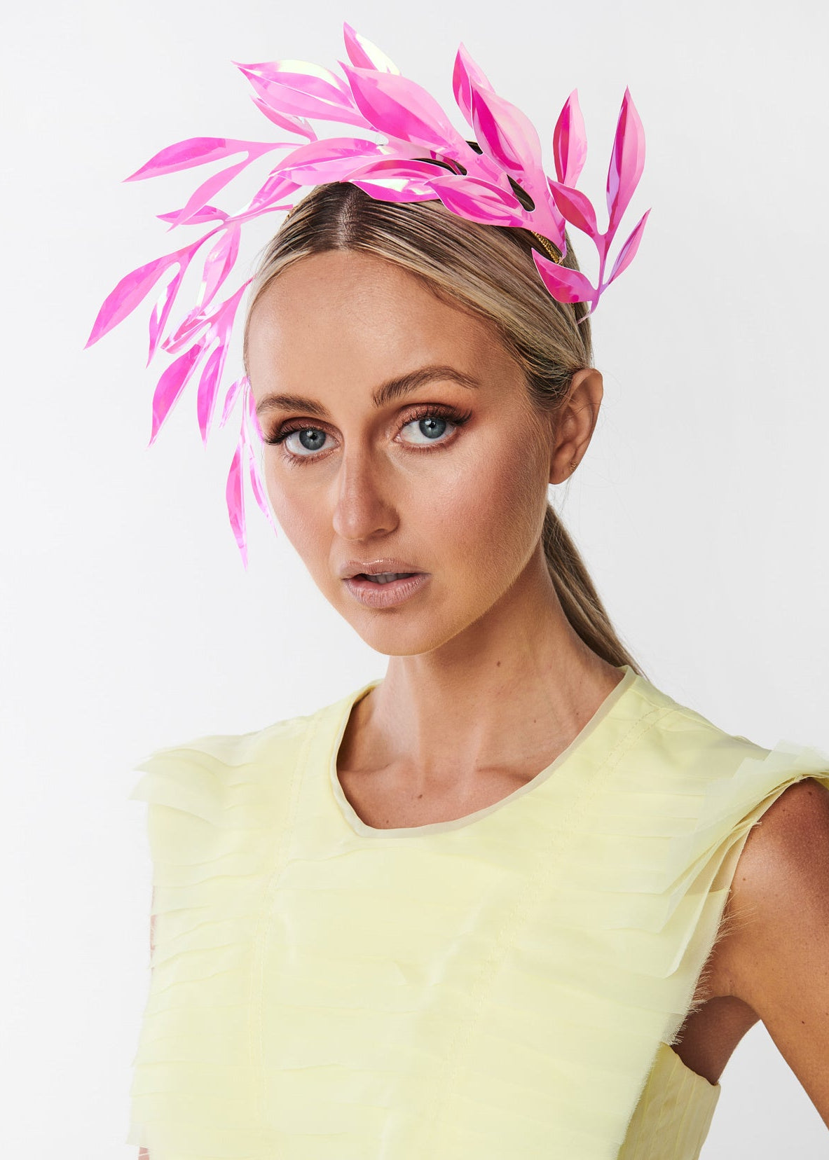 Woman wearing a yellow dress and pink leaf headpiece against a white background