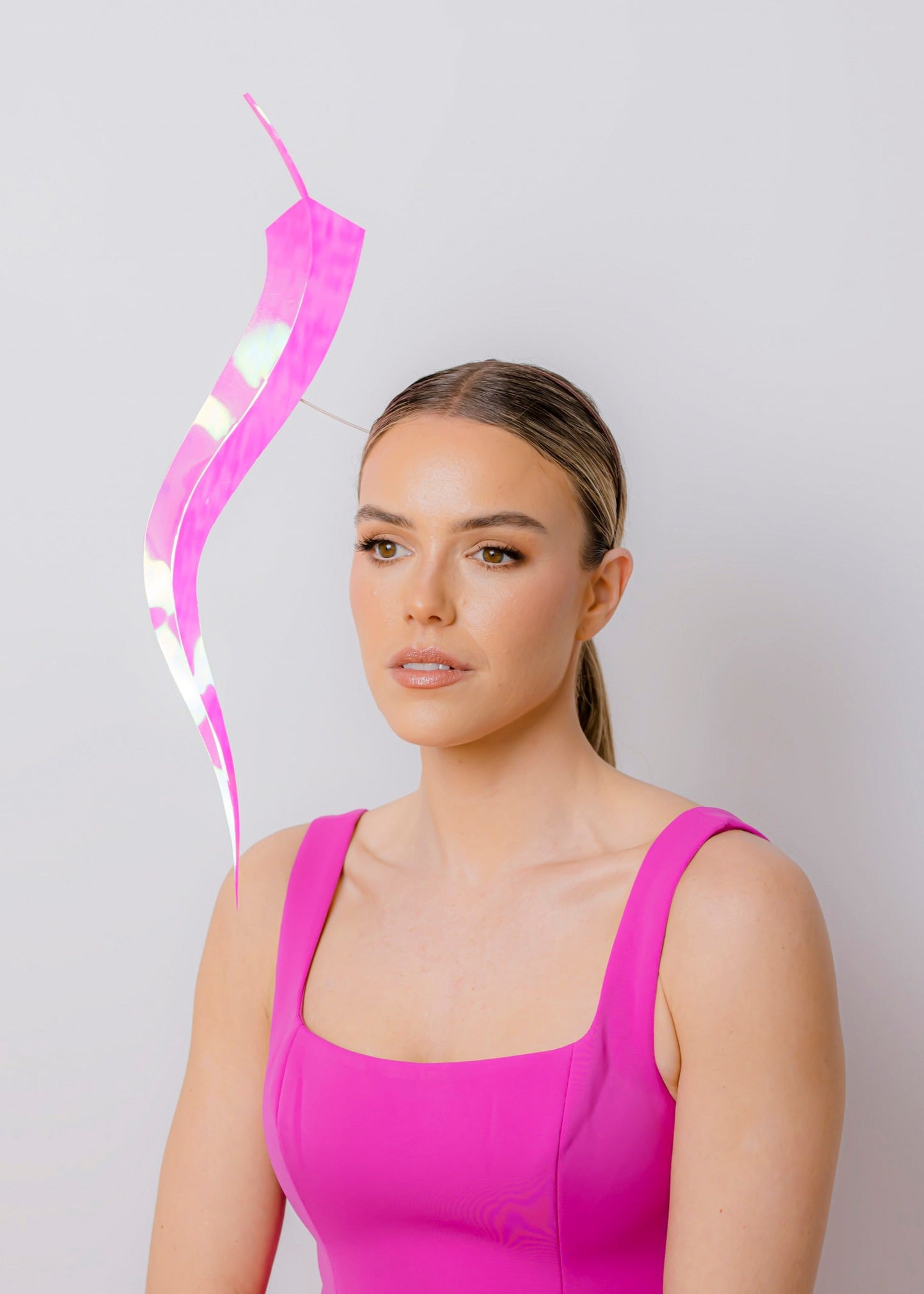 Woman in a pink dress with a long feather headpiece against a light gray background