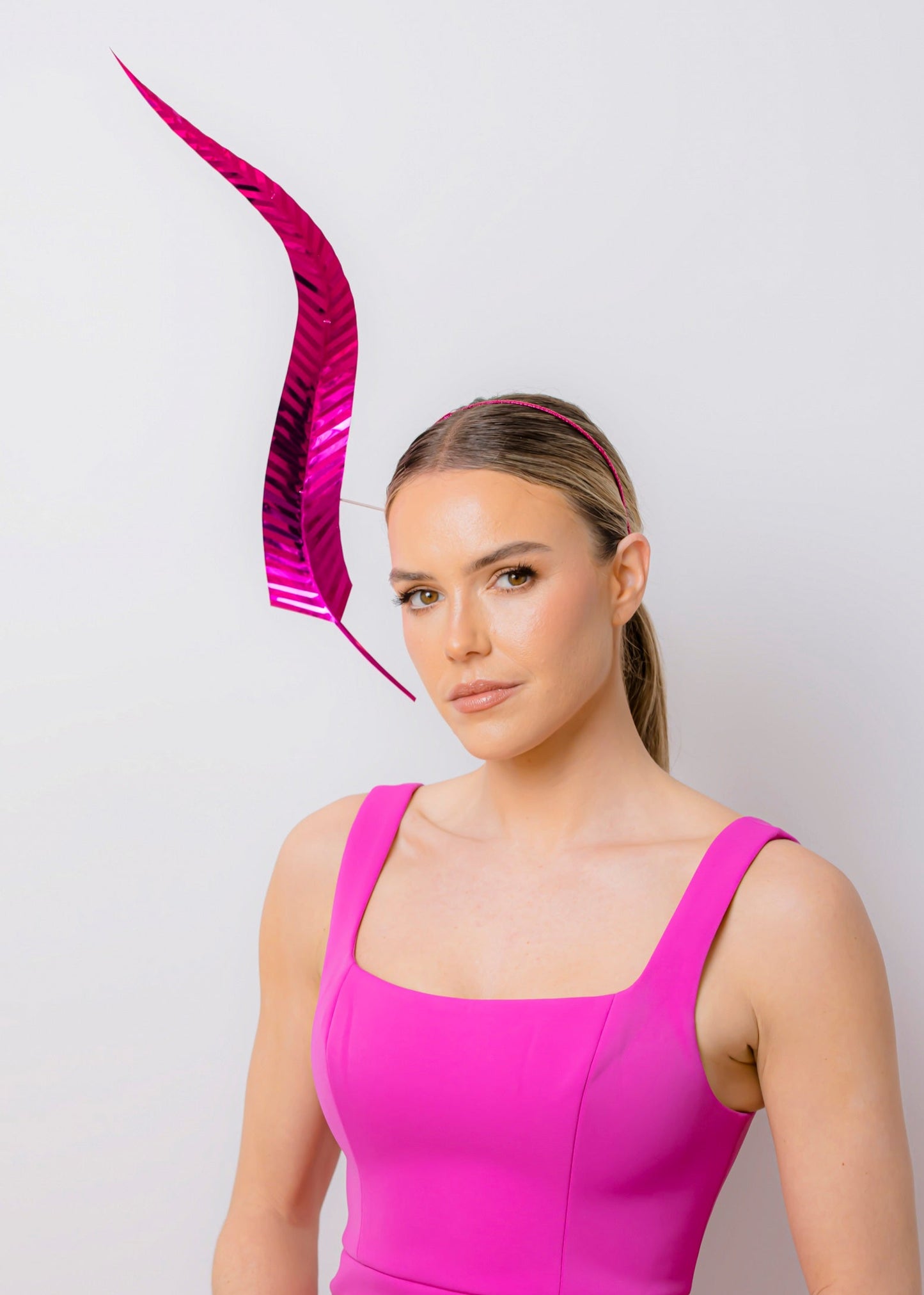 Woman wearing a bright pink dress with a large pink feathered headpiece against a light background