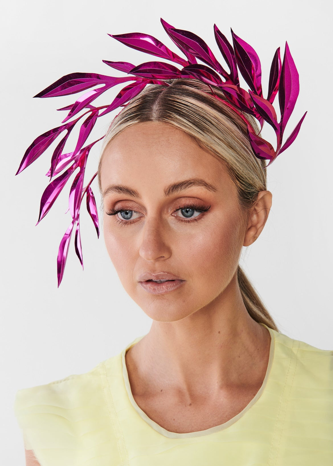 Woman wearing a yellow dress with a decorative leaf headpiece featuring magenta leaves on a white background