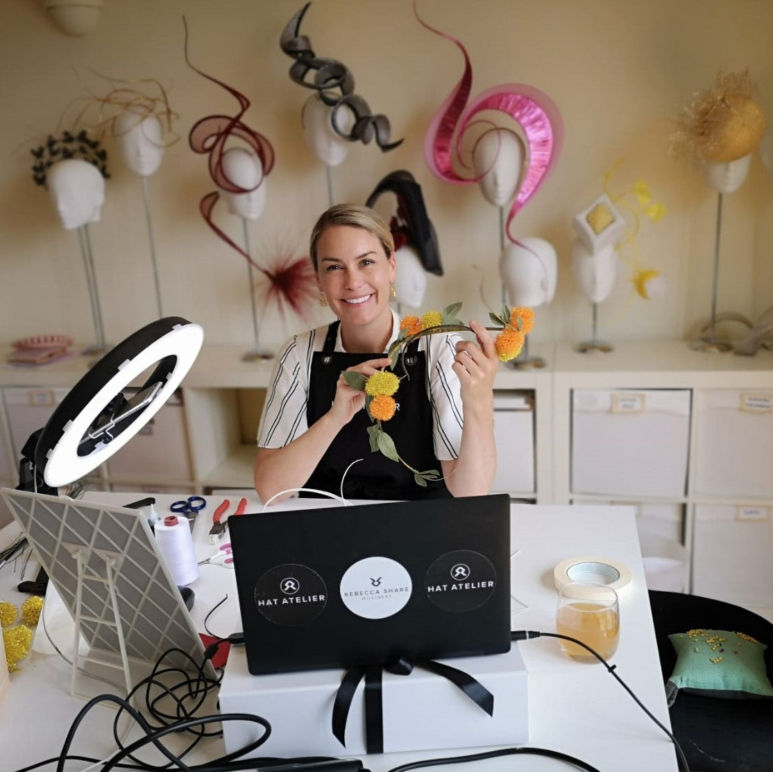 Rebecca Share Milliner in her workshop studio holding yellow and orange designer piece