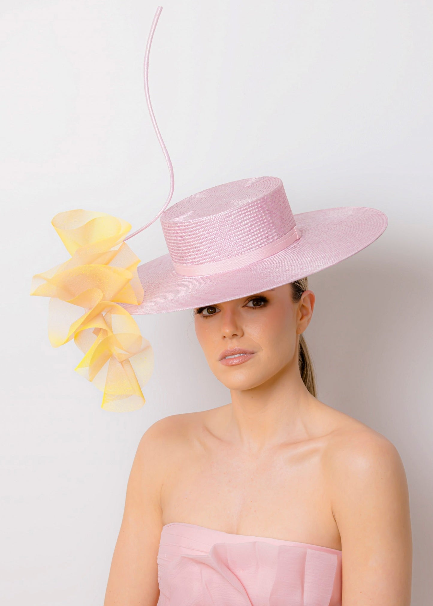 Woman wearing a pink dress and hat with yellow floral trim against a white background