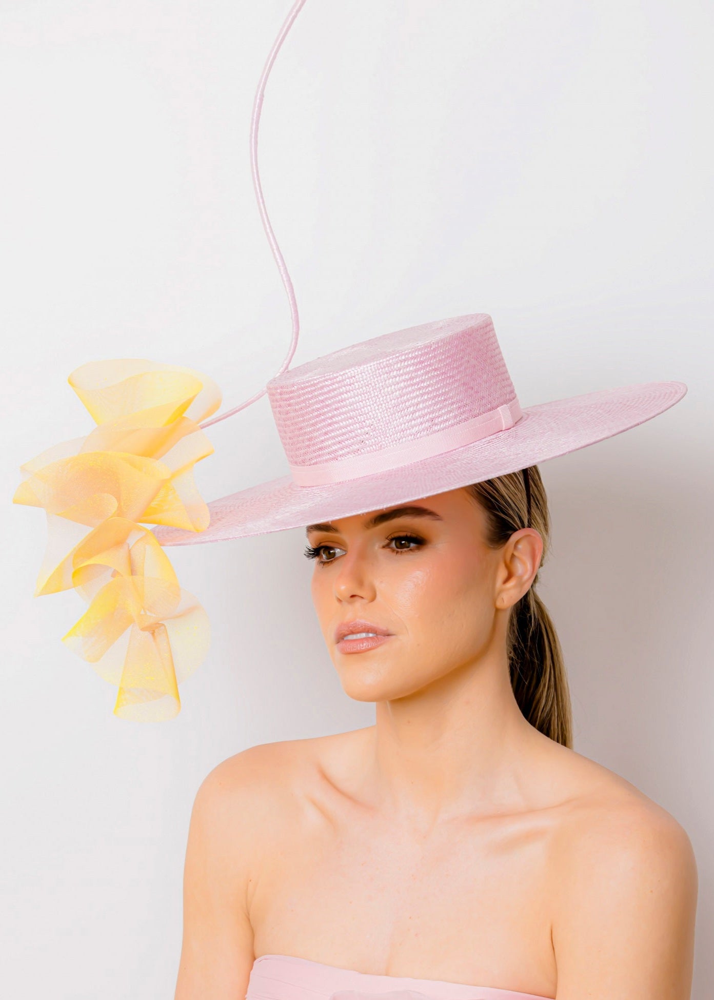 Woman wearing a pink dress and hat with a yellow floral trim against a white background