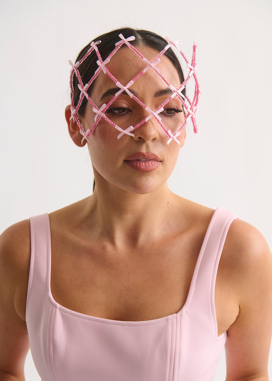 Woman wearing a pink face veil with a lattice design on a white background