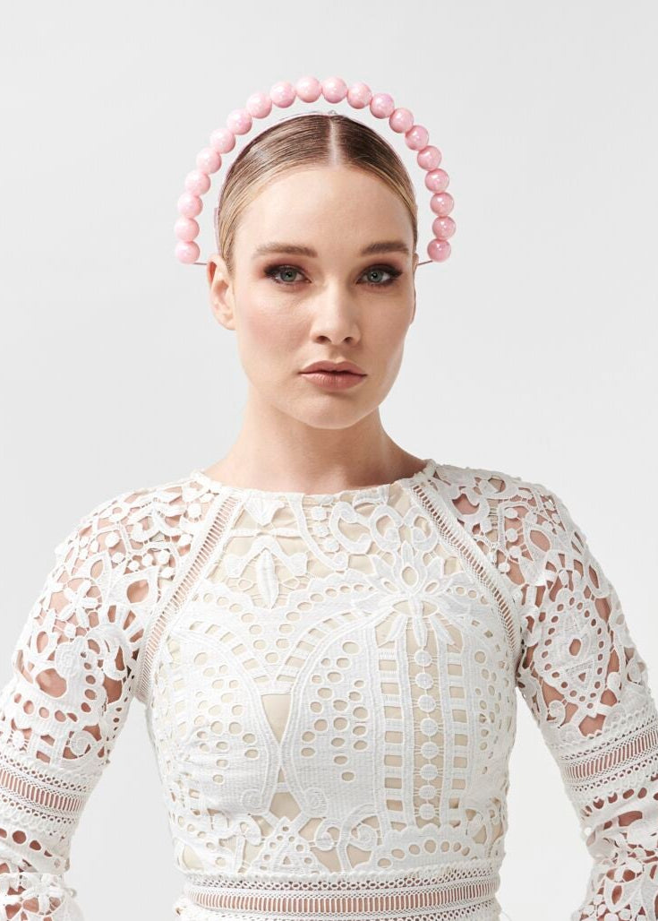 Woman wearing a white lace dress with a pink beaded headband on a light gray background