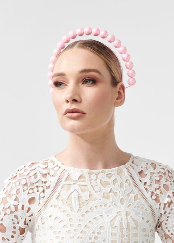 Woman wearing a white lace dress with a pink beaded headband on a light gray background