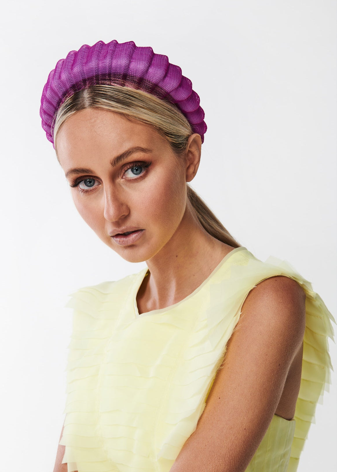 Woman wearing a yellow dress and purple headband against a white background