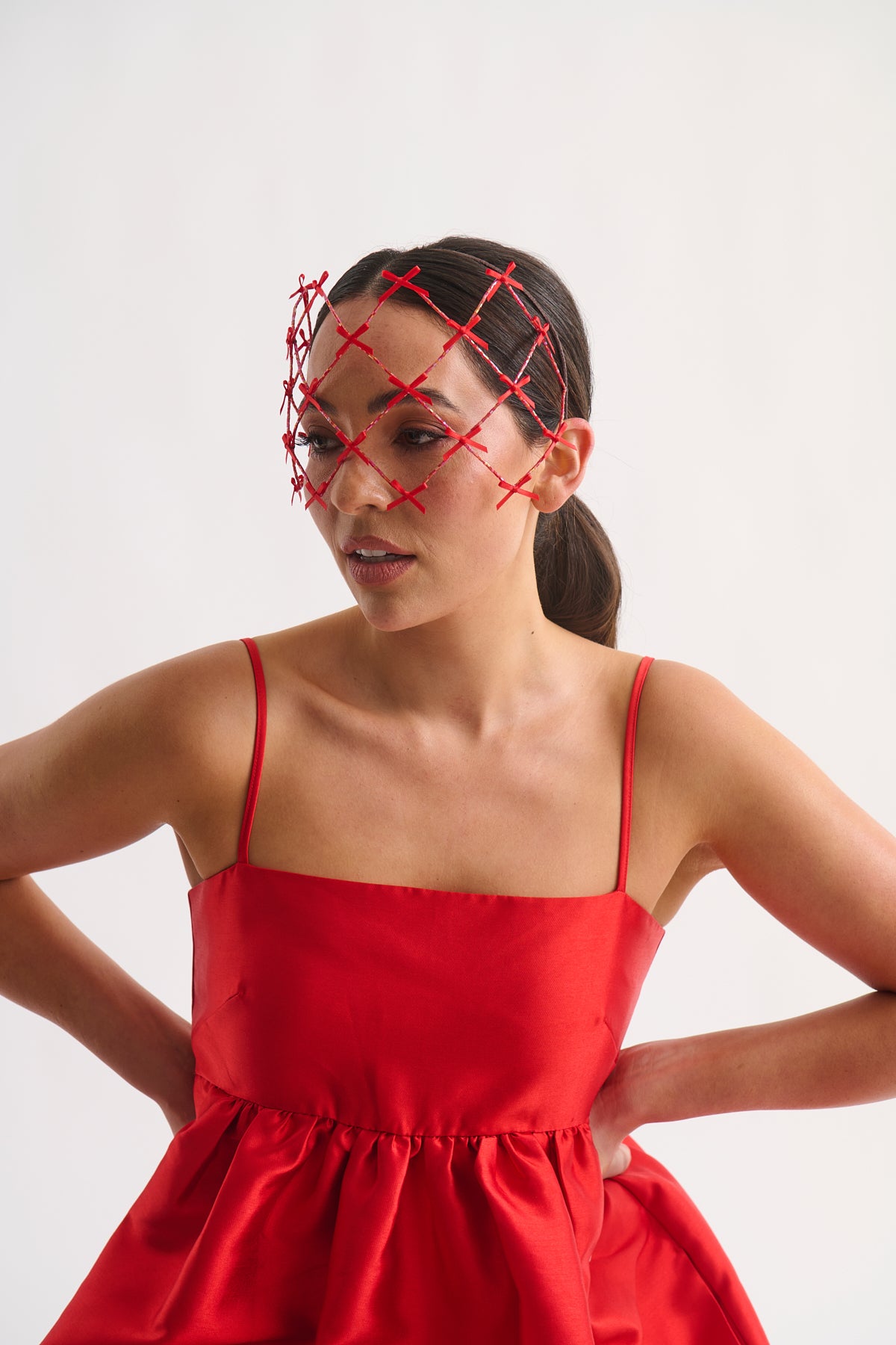 Woman wearing a red dress with a red face veil against a white background