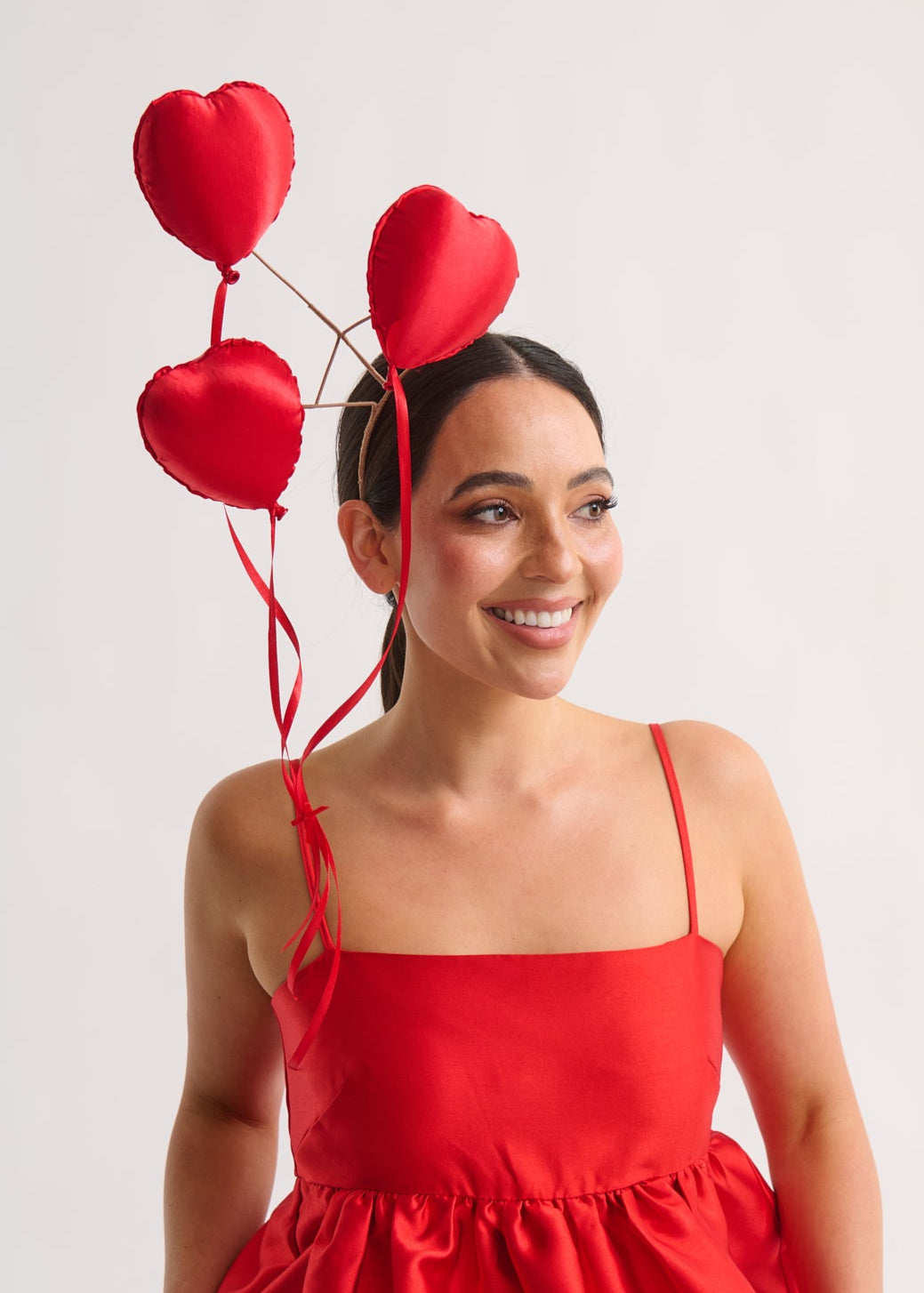 Woman in a red dress with heart-shaped balloons on a plain background