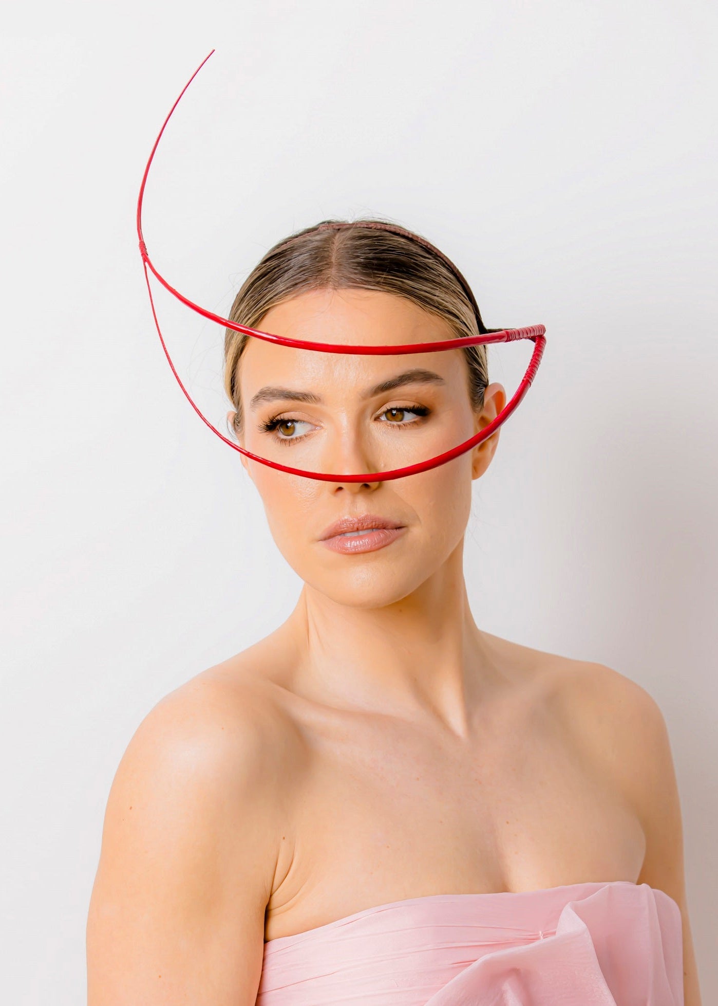 Woman wearing a strapless pink dress with a red circular object above her head against a white background
