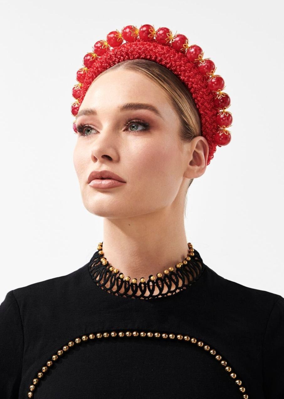 Woman wearing a red headpiece and black outfit with gold details on a white background