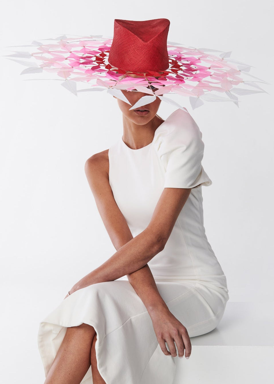 Woman wearing a white dress and a large red and pink hat on a white background
