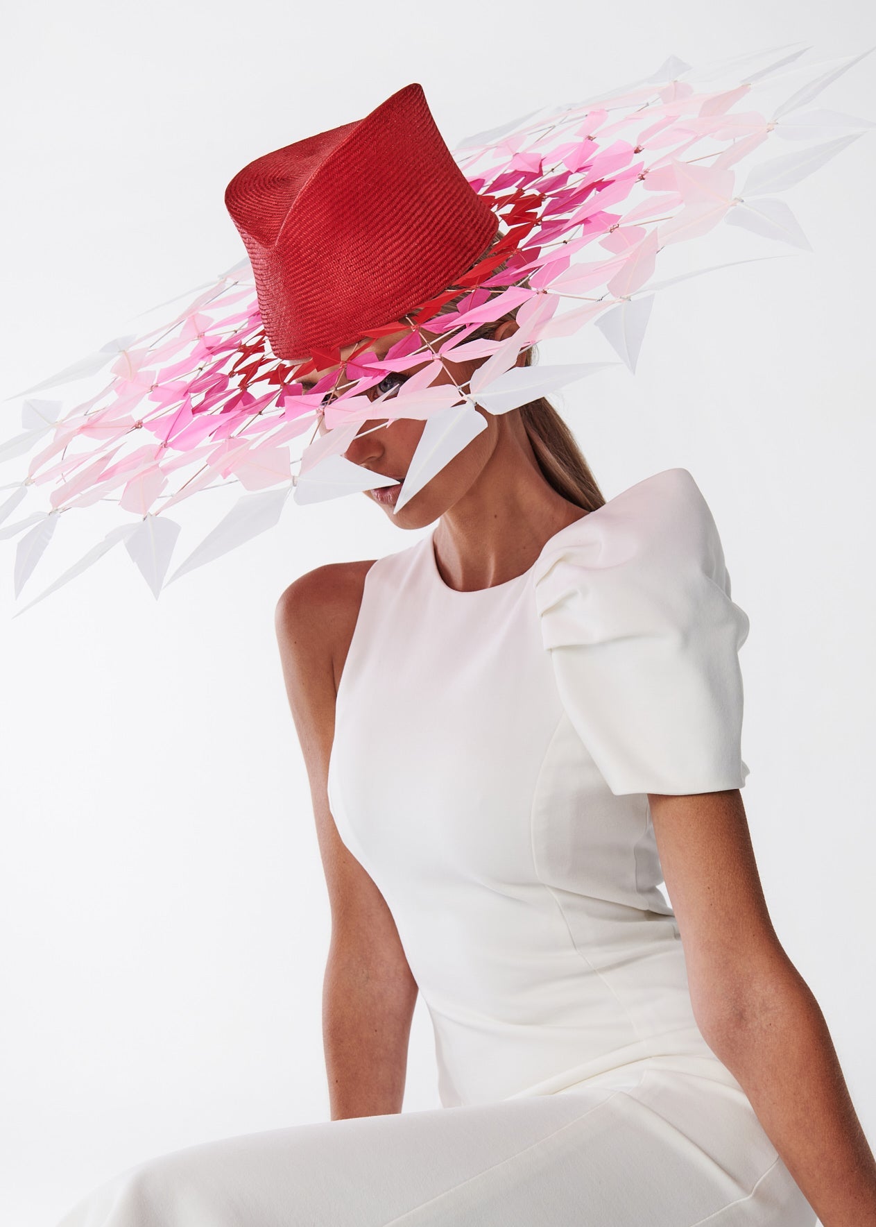 Woman wearing a white dress and red hat with pink feathers against a white background