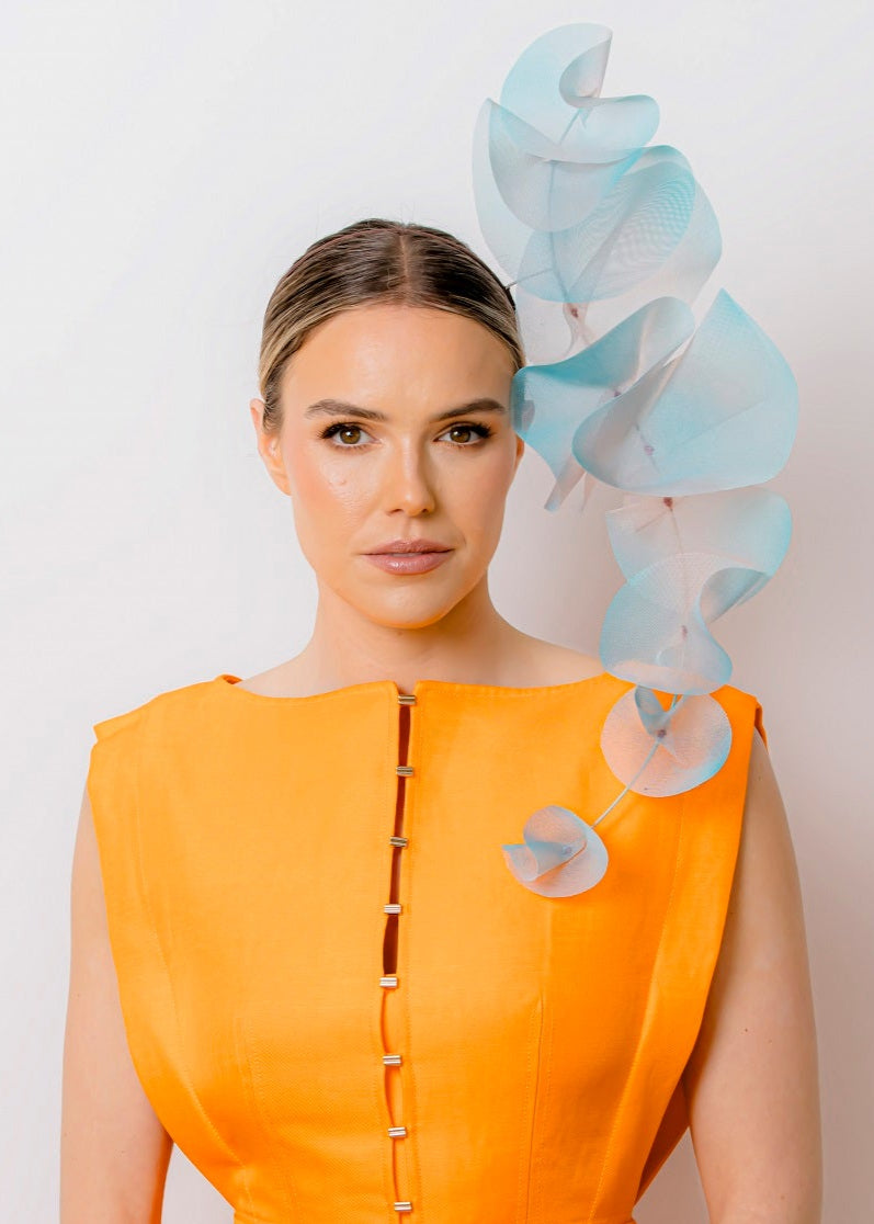 Woman wearing an orange dress with a decorative headpiece against a plain background