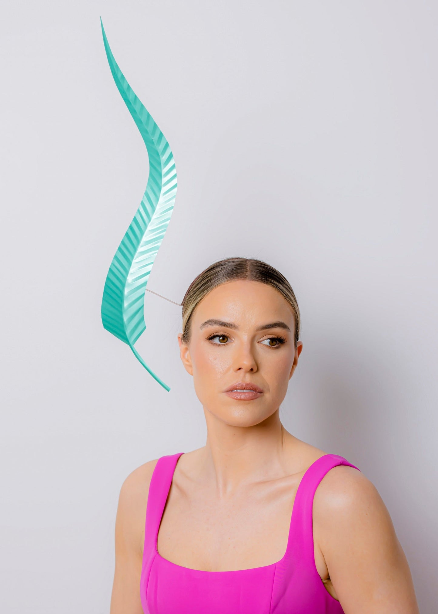 Woman wearing a bright pink dress and long feather headpiece against a light gray background