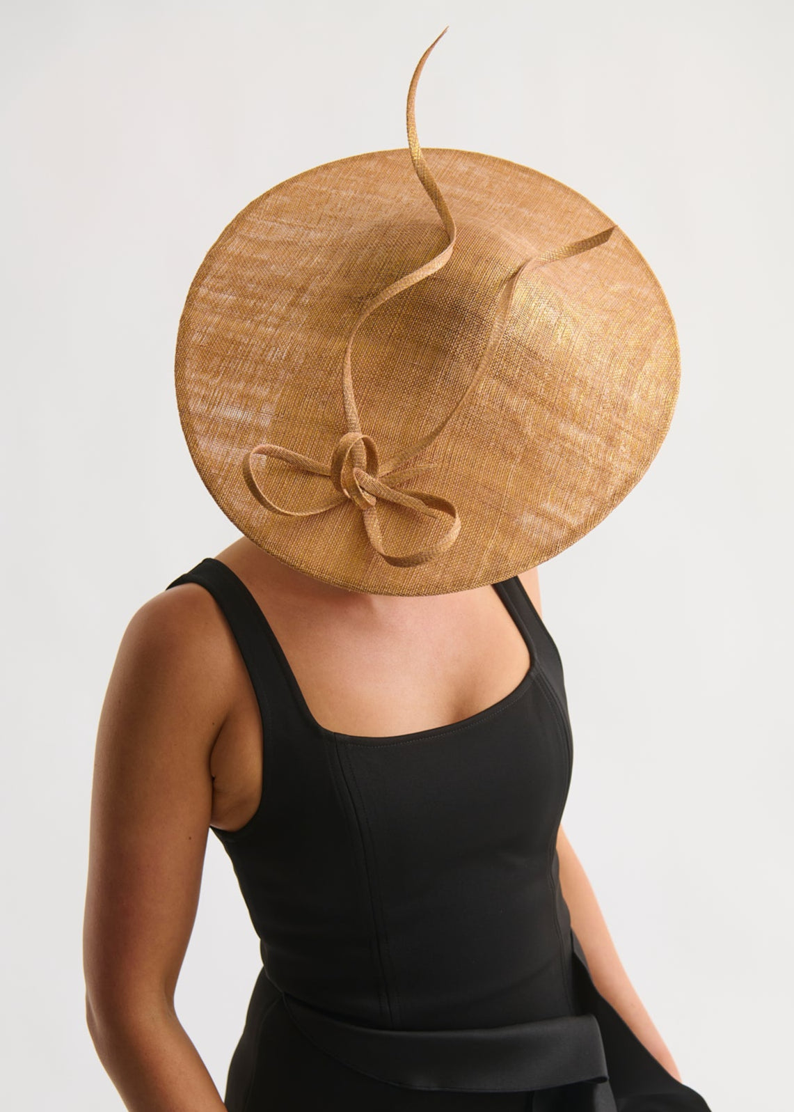 Person wearing a large straw hat with a bow on a plain background