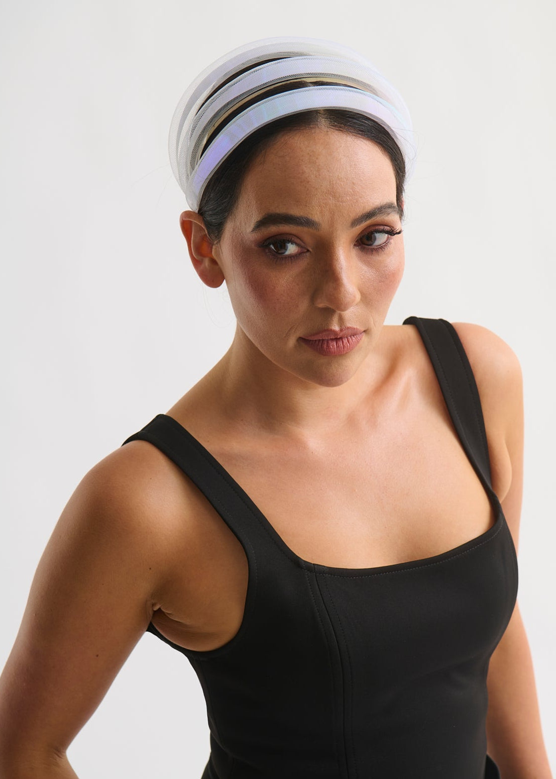 Woman wearing a black sleeveless top with a white headband on a plain background