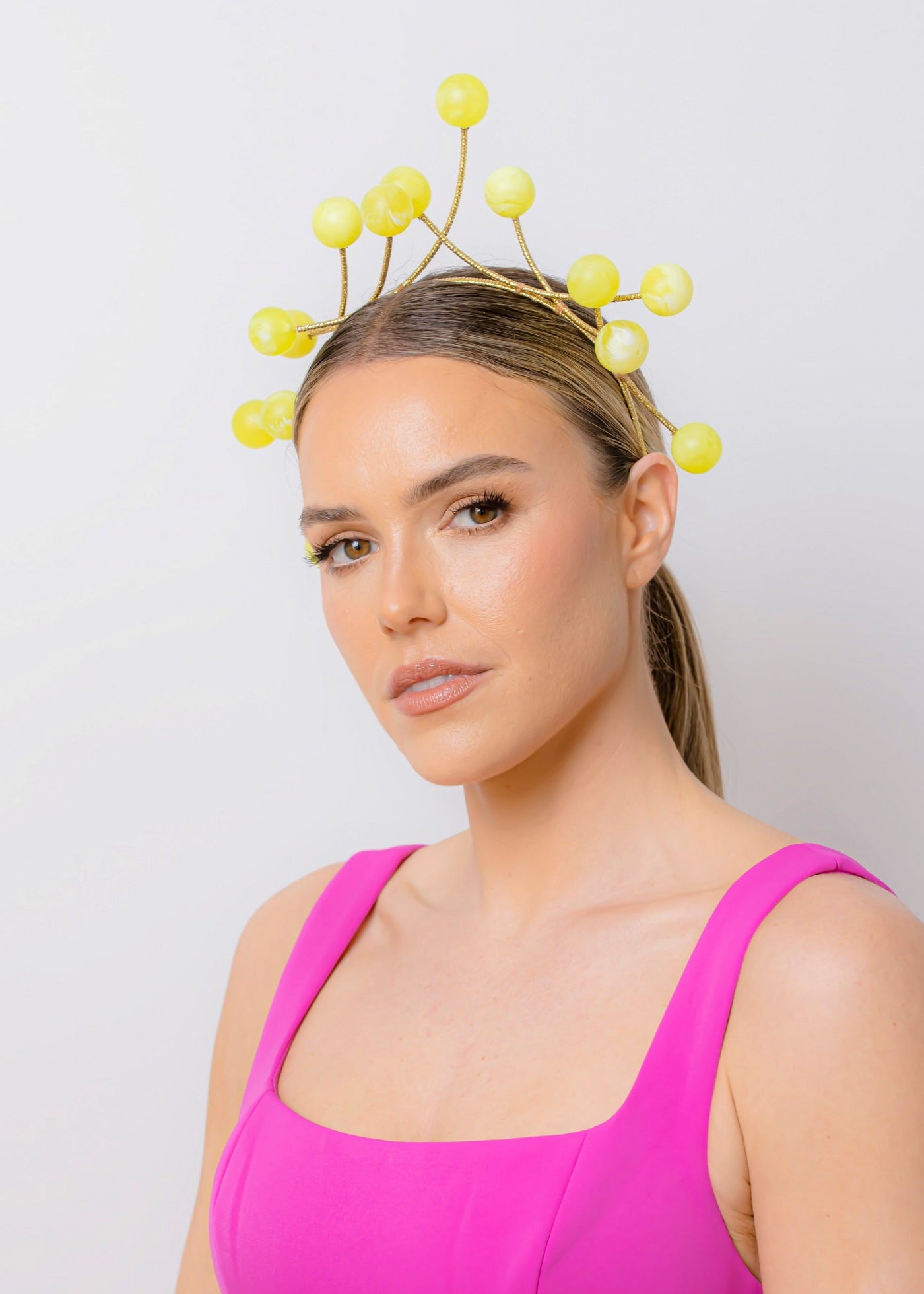 Woman wearing a bright pink dress and a decorative yellow headpiece against a light gray background
