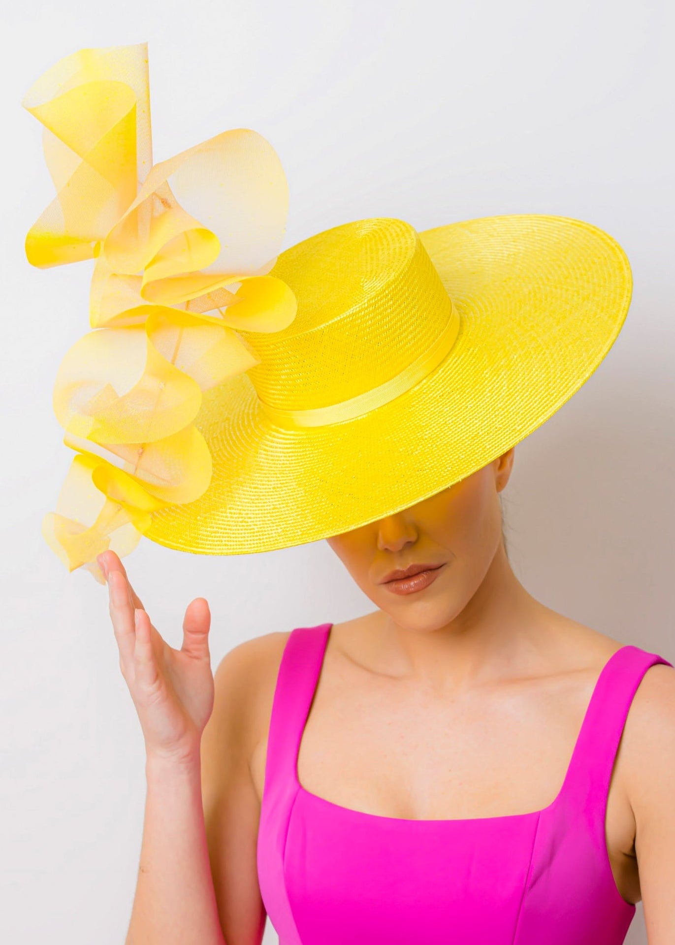 Woman wearing a bright yellow hat with ruffles and a pink dress against a white background