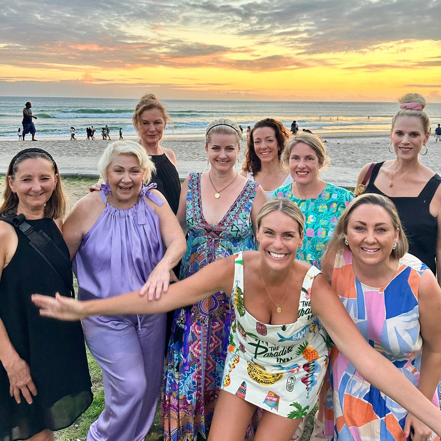 Group of women posing for a photo on a beach at sunset.