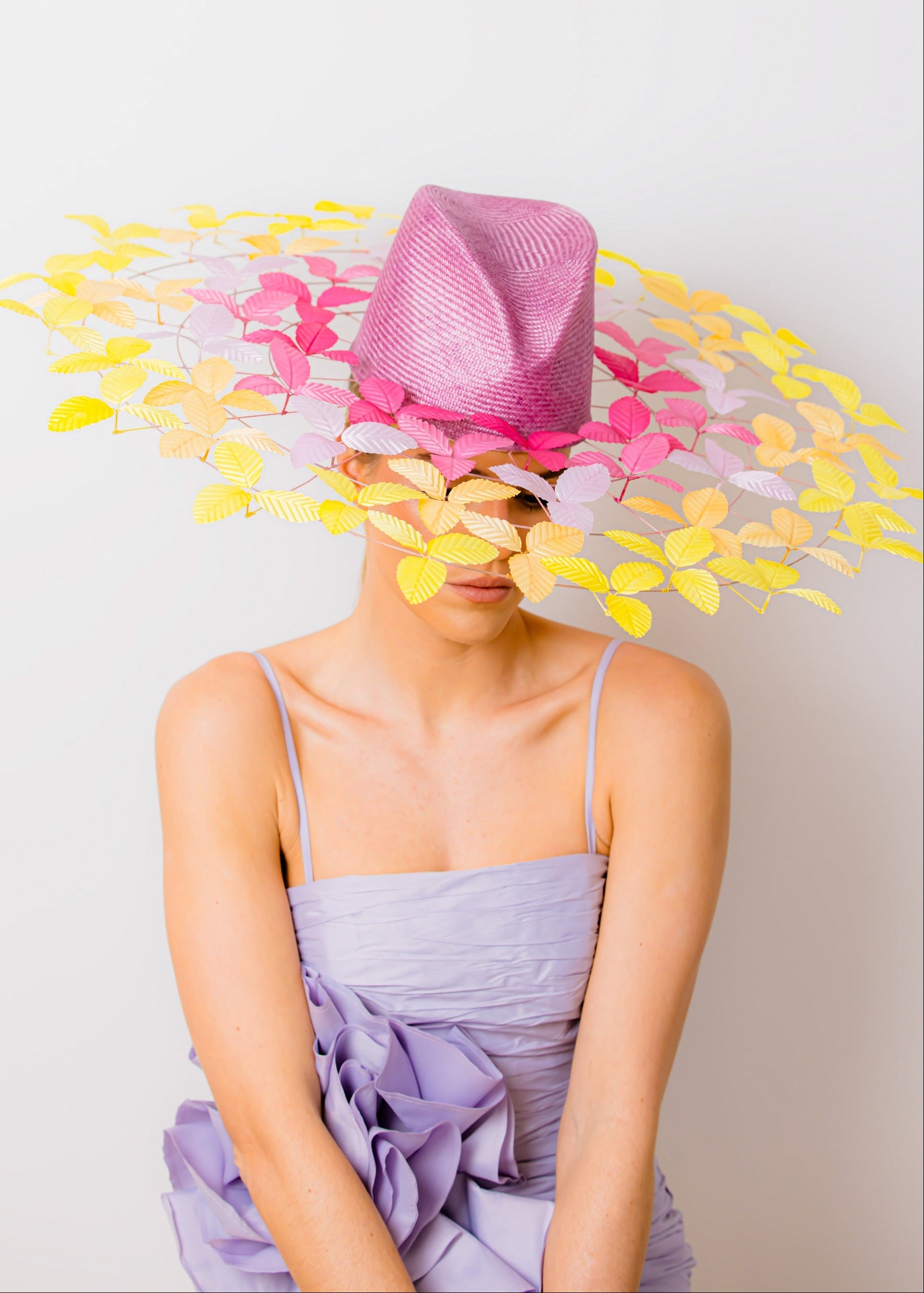 Person wearing a colorful hat with flowers and a purple dress against a white background