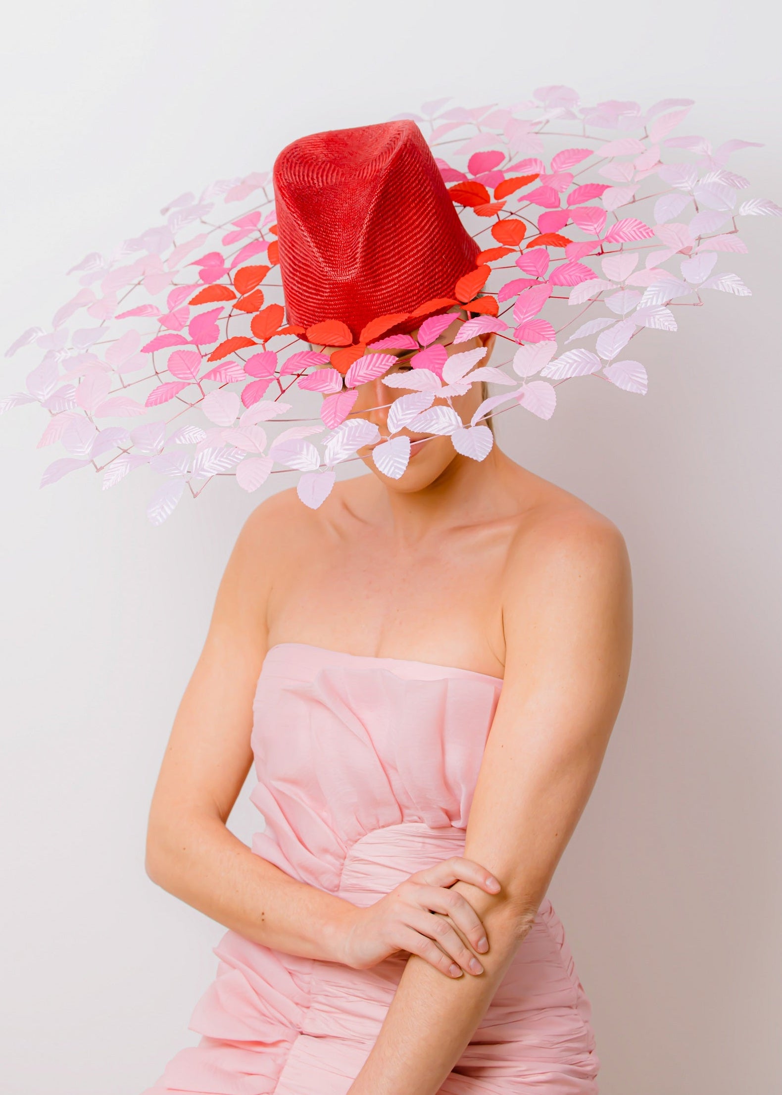 Person wearing a vibrant red hat with floral decorations on a plain background