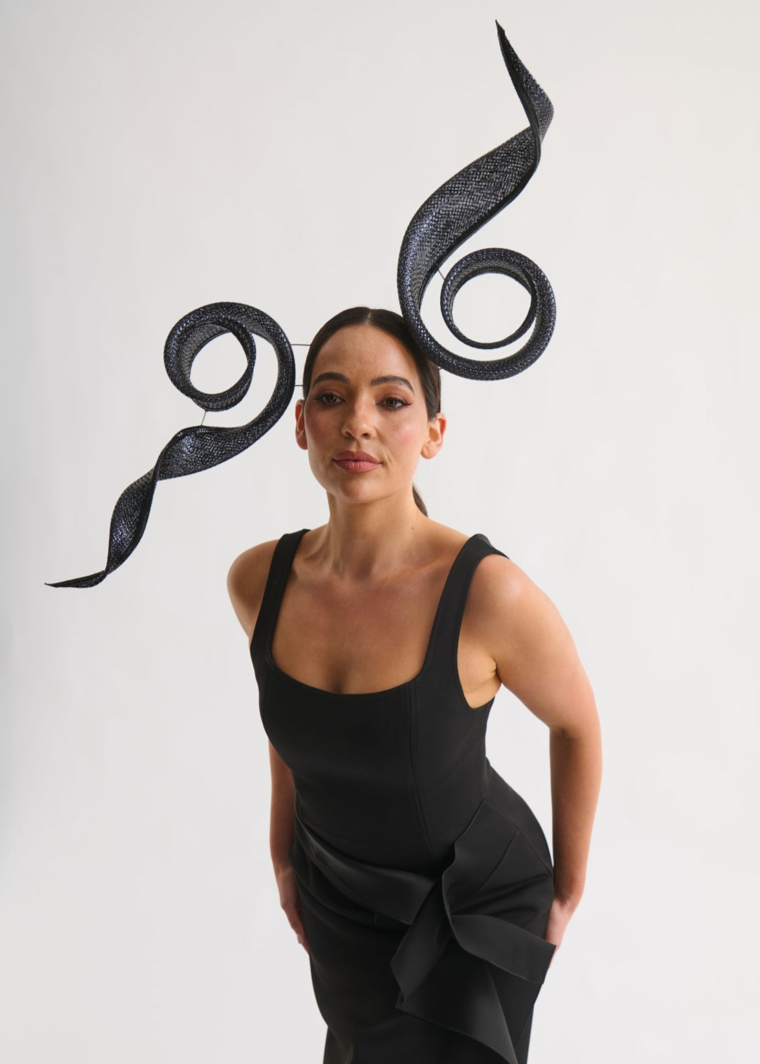Woman wearing a black dress with large swirl headpiece on a white background