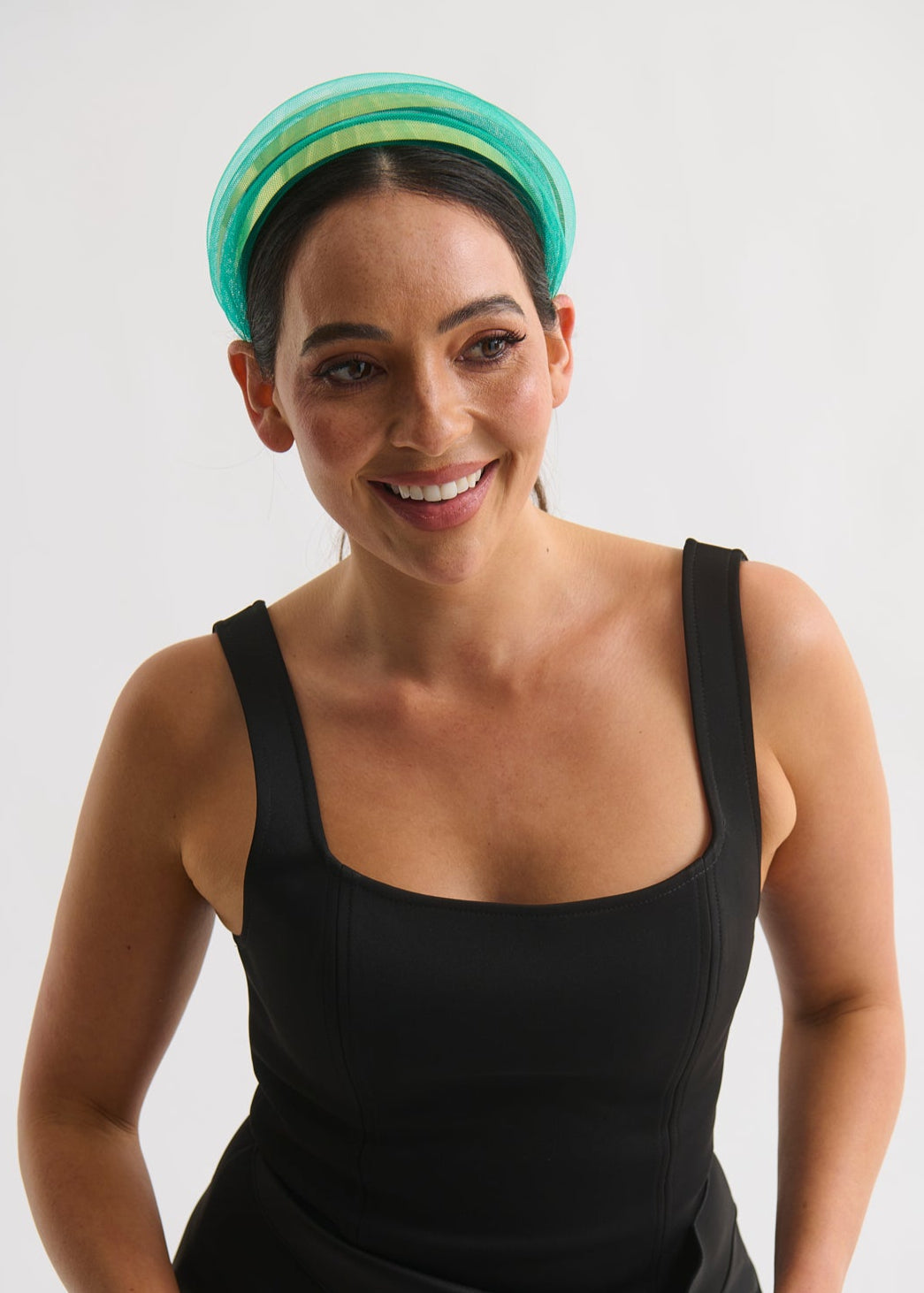 Woman wearing a black sleeveless dress and green headband against a white background