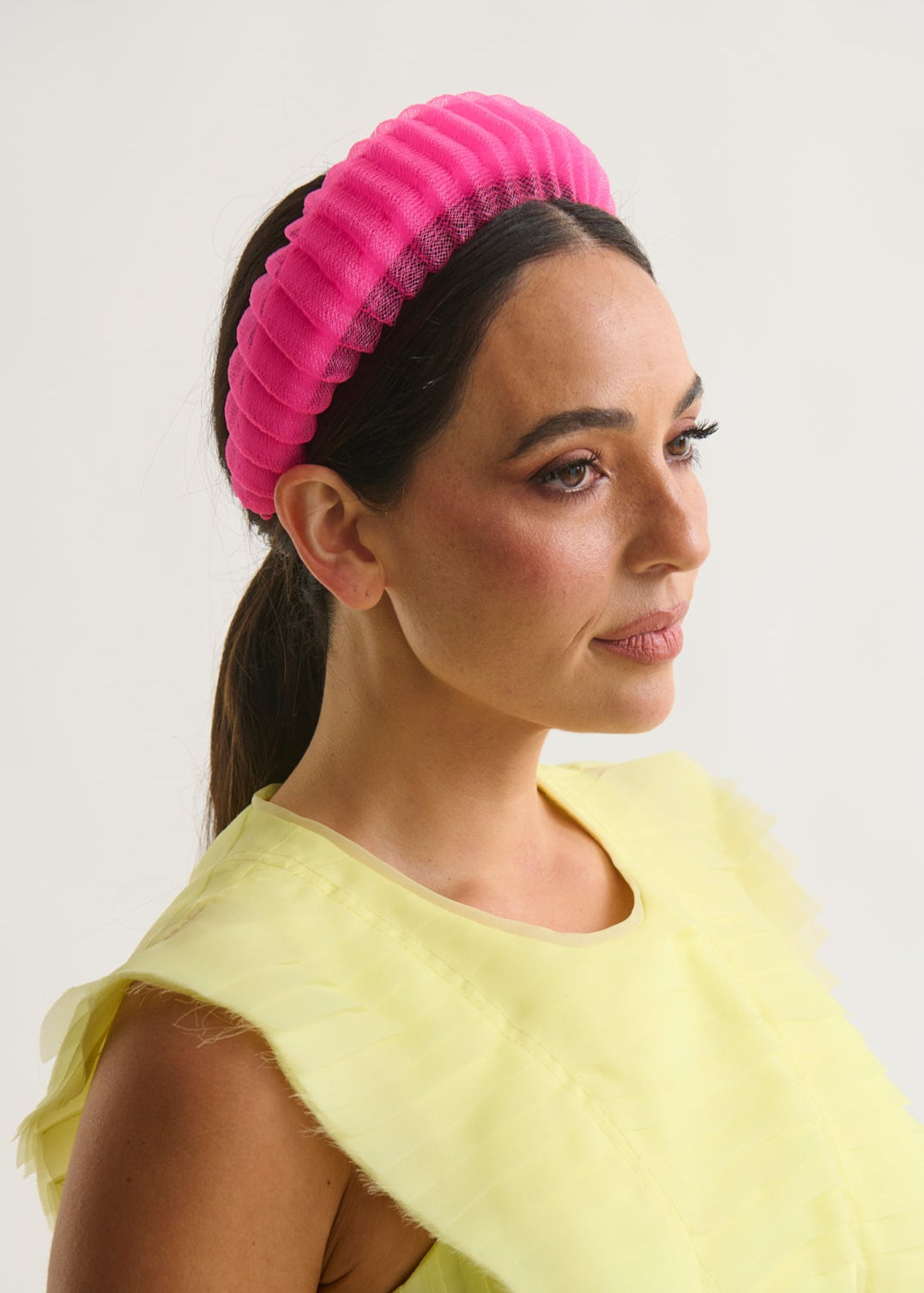 Woman wearing a bright pink headband and a yellow top against a white background