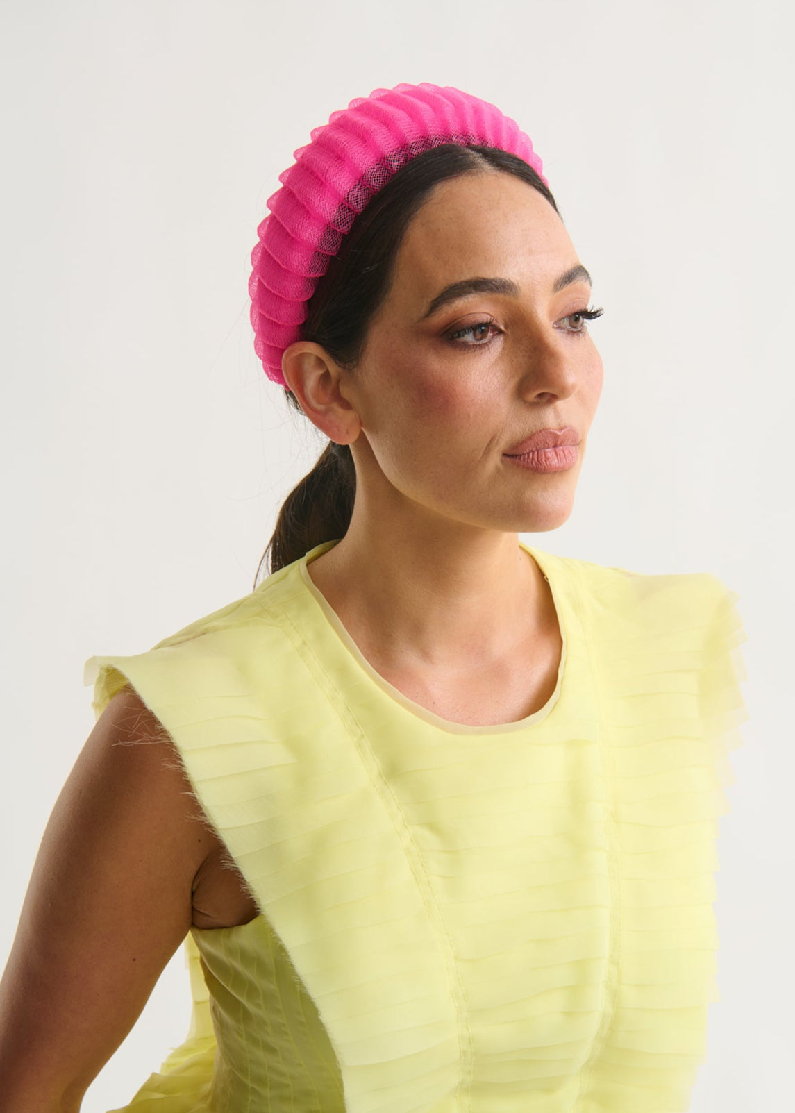 Woman wearing a bright pink headband and a yellow dress against a white background