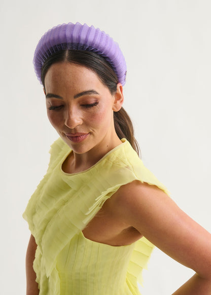 Woman wearing a yellow dress and purple headband against a white background