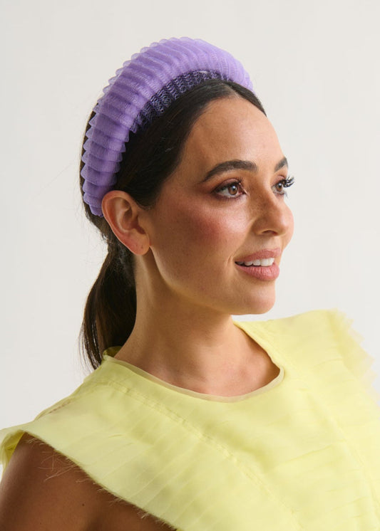 Woman wearing a yellow dress and purple headband against a white background