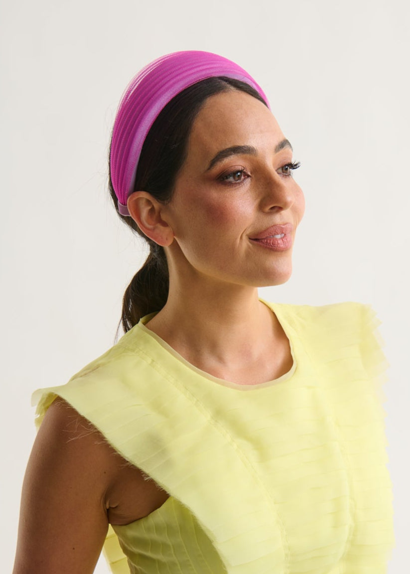 Woman wearing a bright yellow dress and magenta headband against a white background