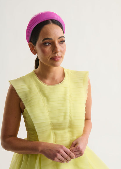 Woman wearing a bright yellow dress and magenta headband against a white background