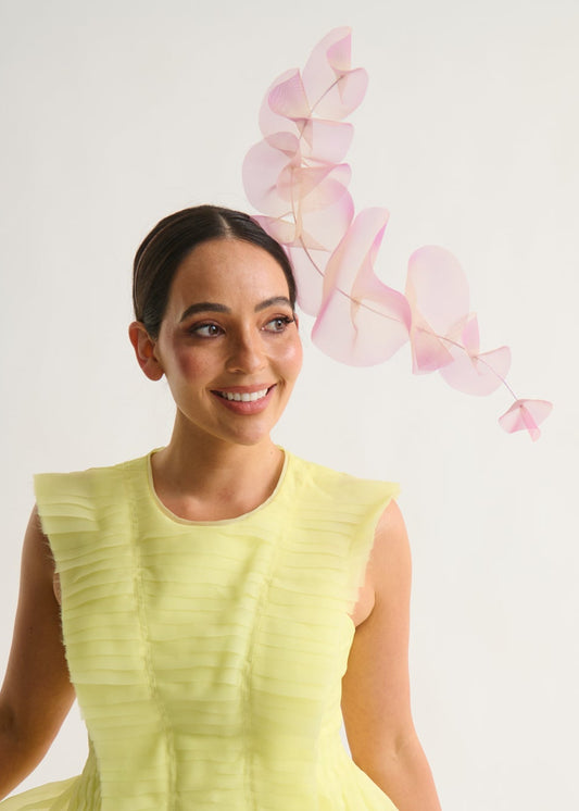 Woman wearing a lilac ruffle headpiece and a yellow dress against a white background