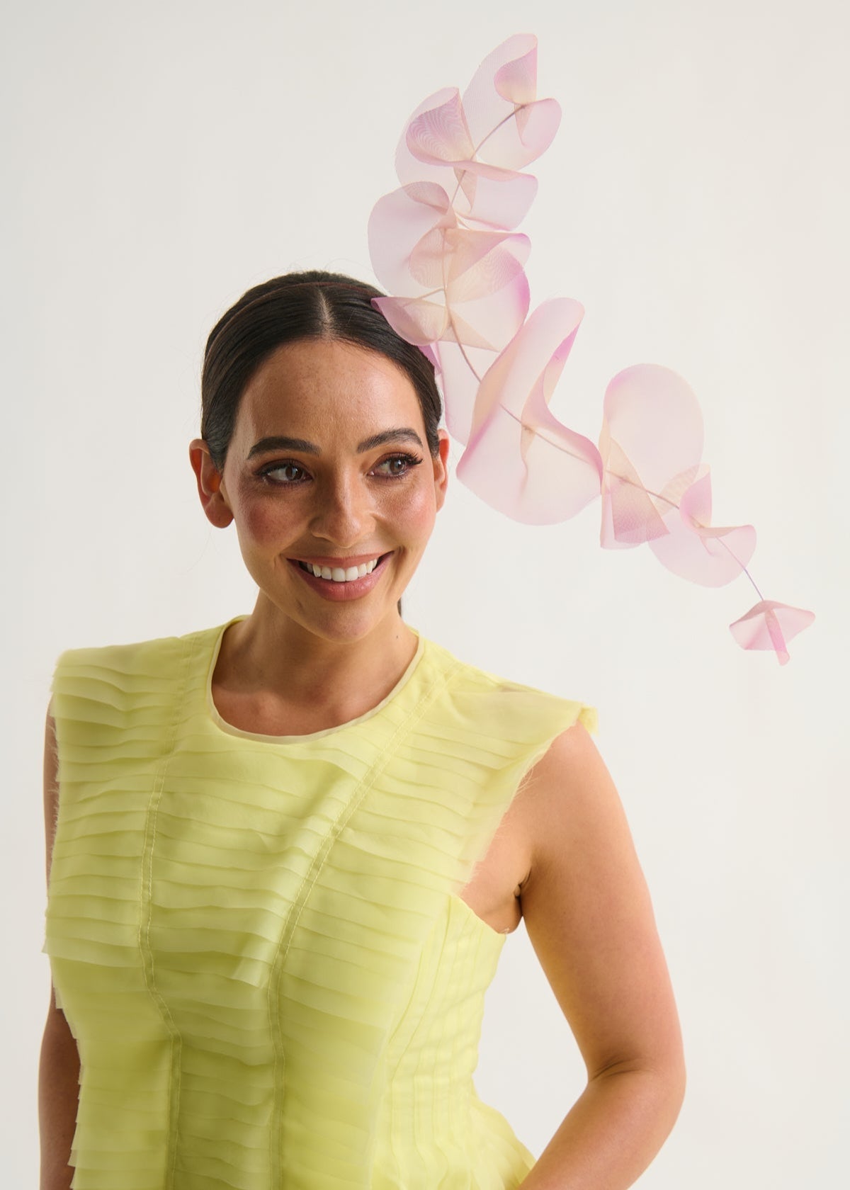 Woman wearing a lilac ruffle headpiece and a yellow dress against a white background