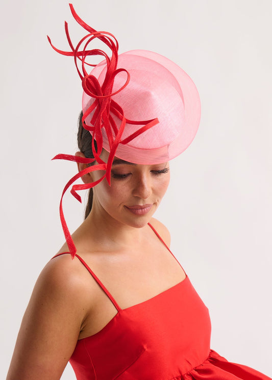 Woman wearing a red dress and pink fascinator with red decorations on a white background