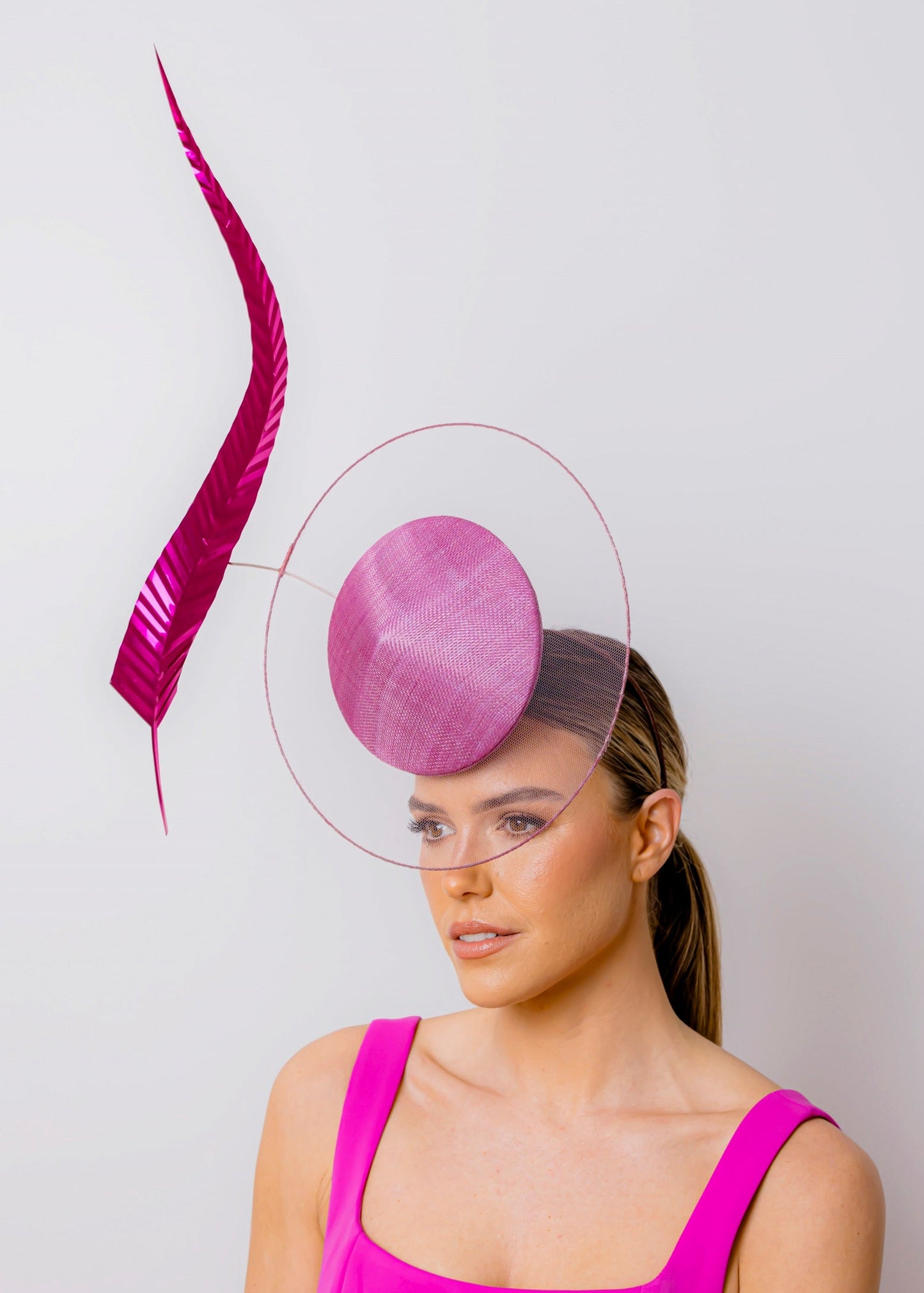 Woman wearing a pink dress and hat with a decorative feather against a light grey background