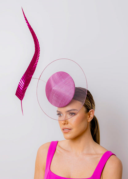 Woman wearing a pink dress and hat with a decorative feather against a light grey background