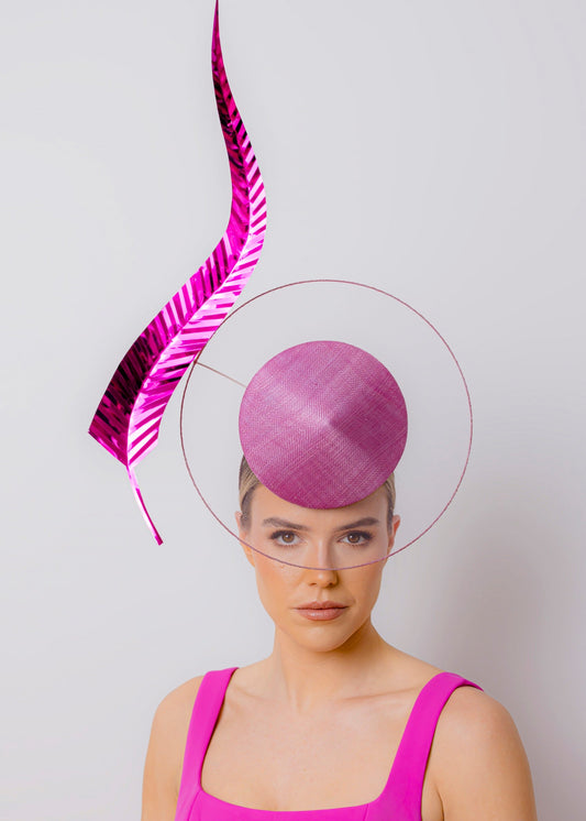 Woman wearing a vibrant pink dress and hat with a large feather against a light gray background