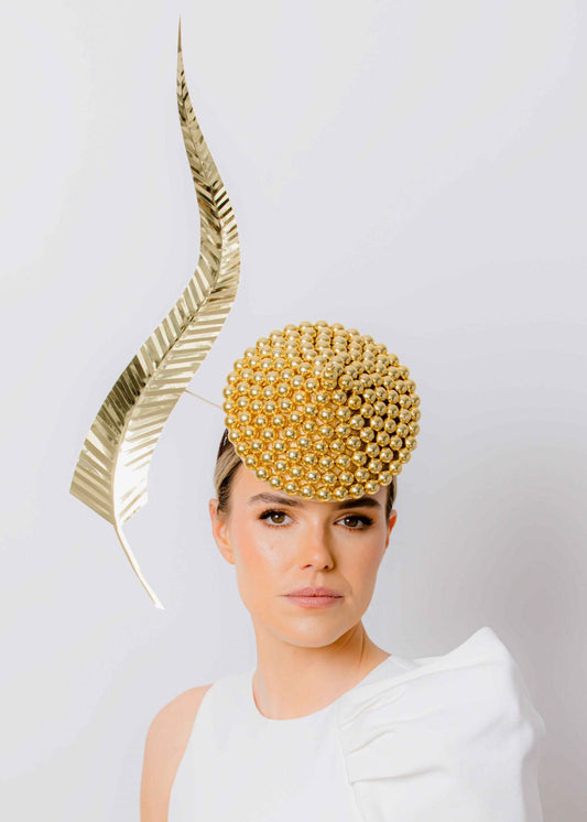 Woman wearing a gold headpiece with a white dress against a plain background