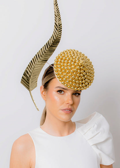 Woman wearing a white dress with a decorative gold headpiece against a plain background