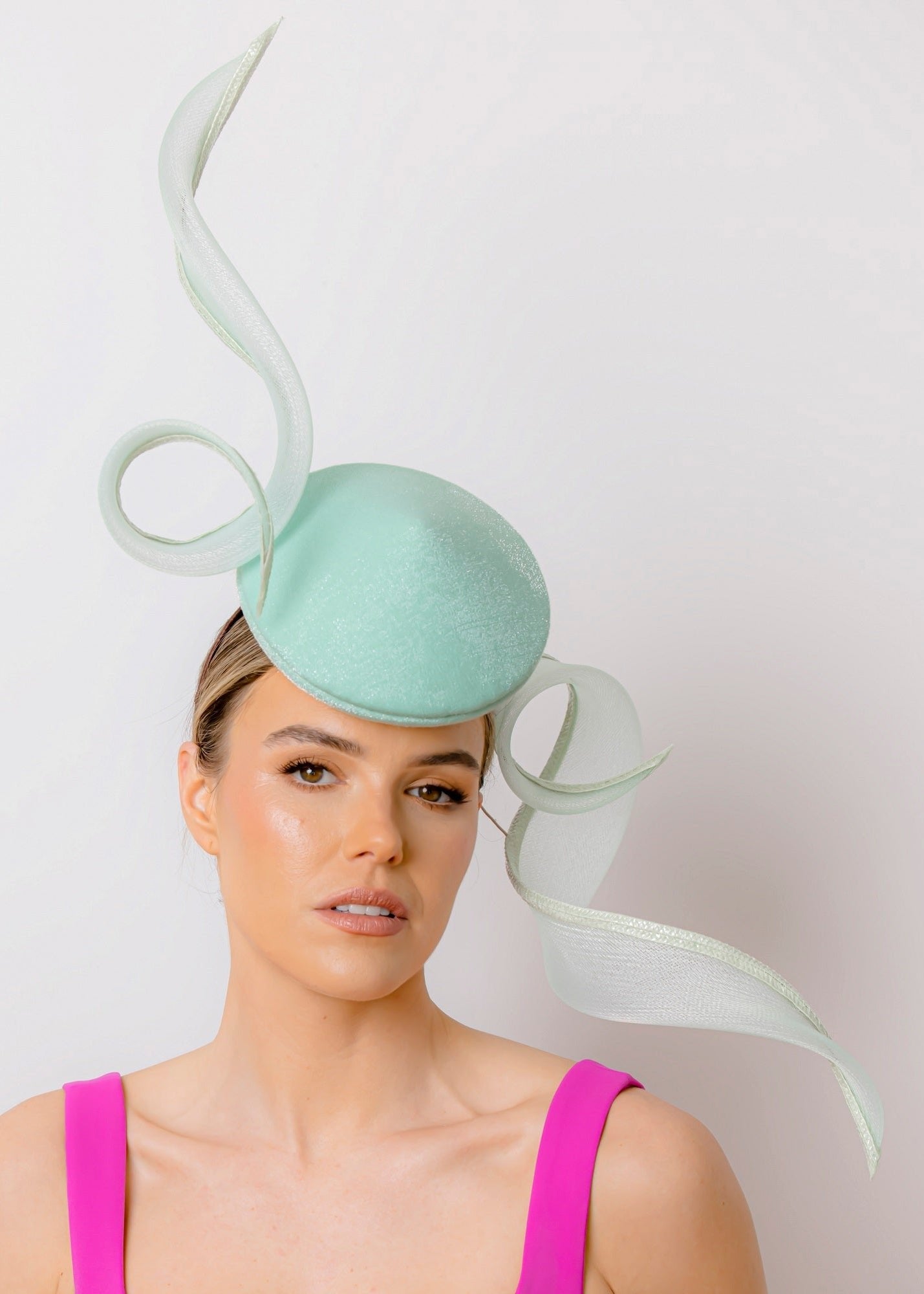 A woman wearing a pastel mint green Percher style hat with a duo of dramatic wired crinoline swirl trims.