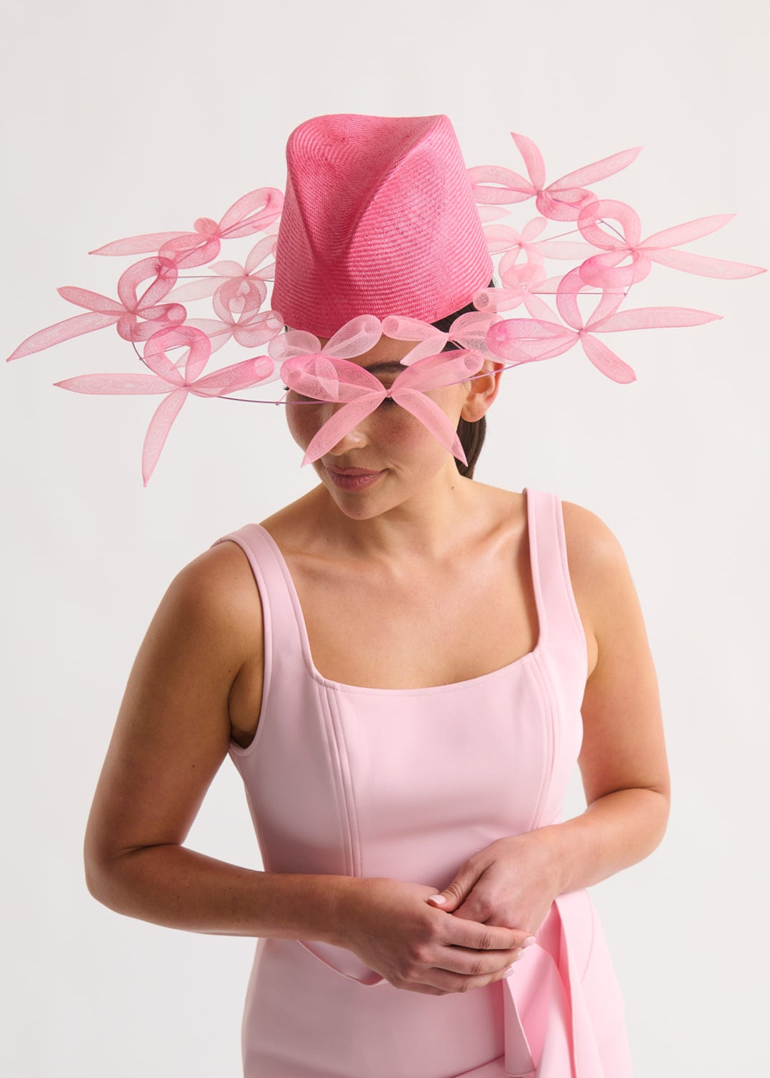 Woman wearing a pink dress and matching hat with bow details on a white background