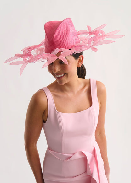 Woman wearing a pink dress and hat with bow details on a white background
