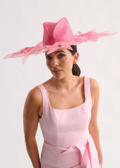 Woman wearing a pink dress and hat against a white background