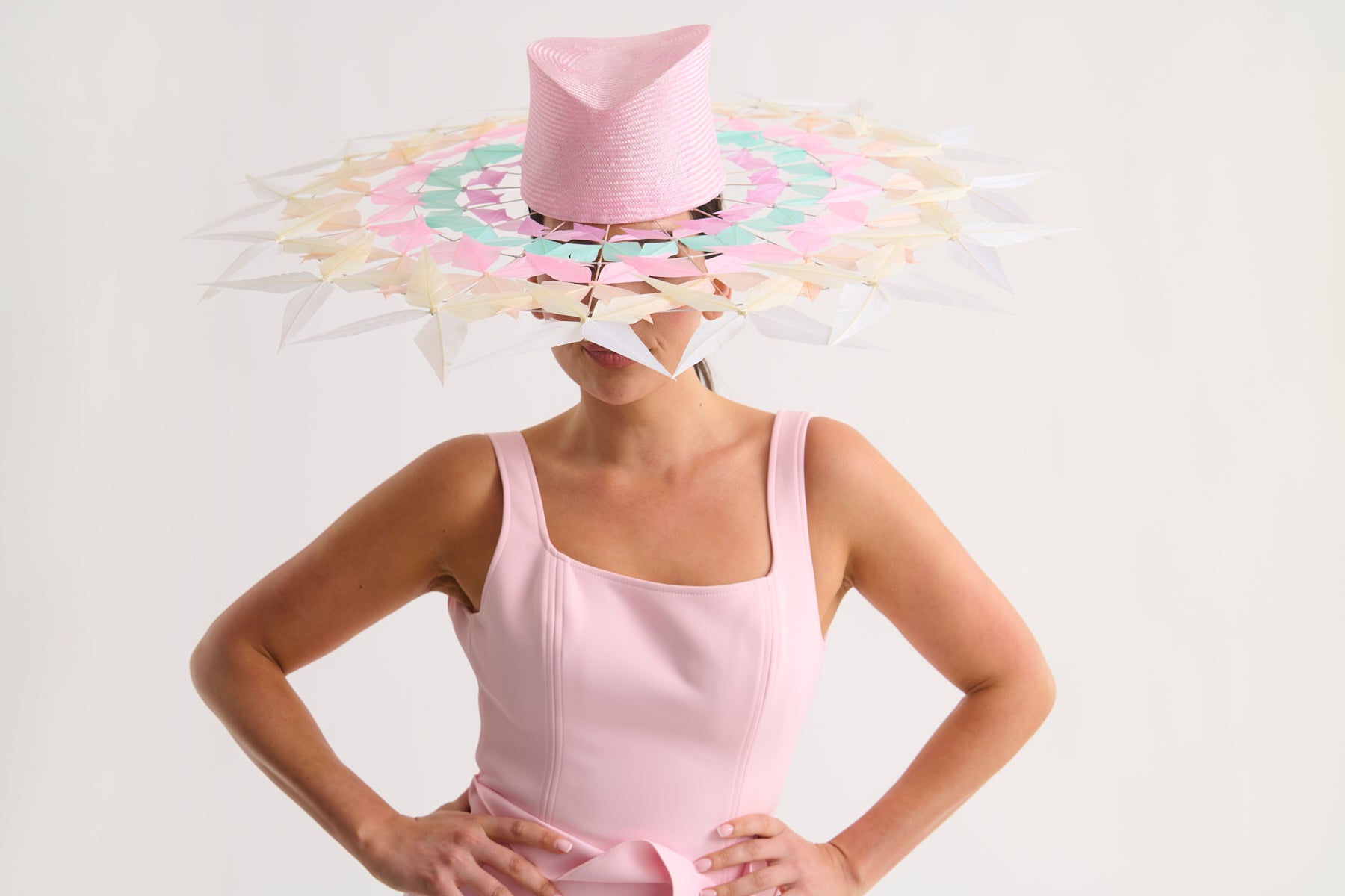 Woman wearing a wide feather brim hat and a pink dress against a white background