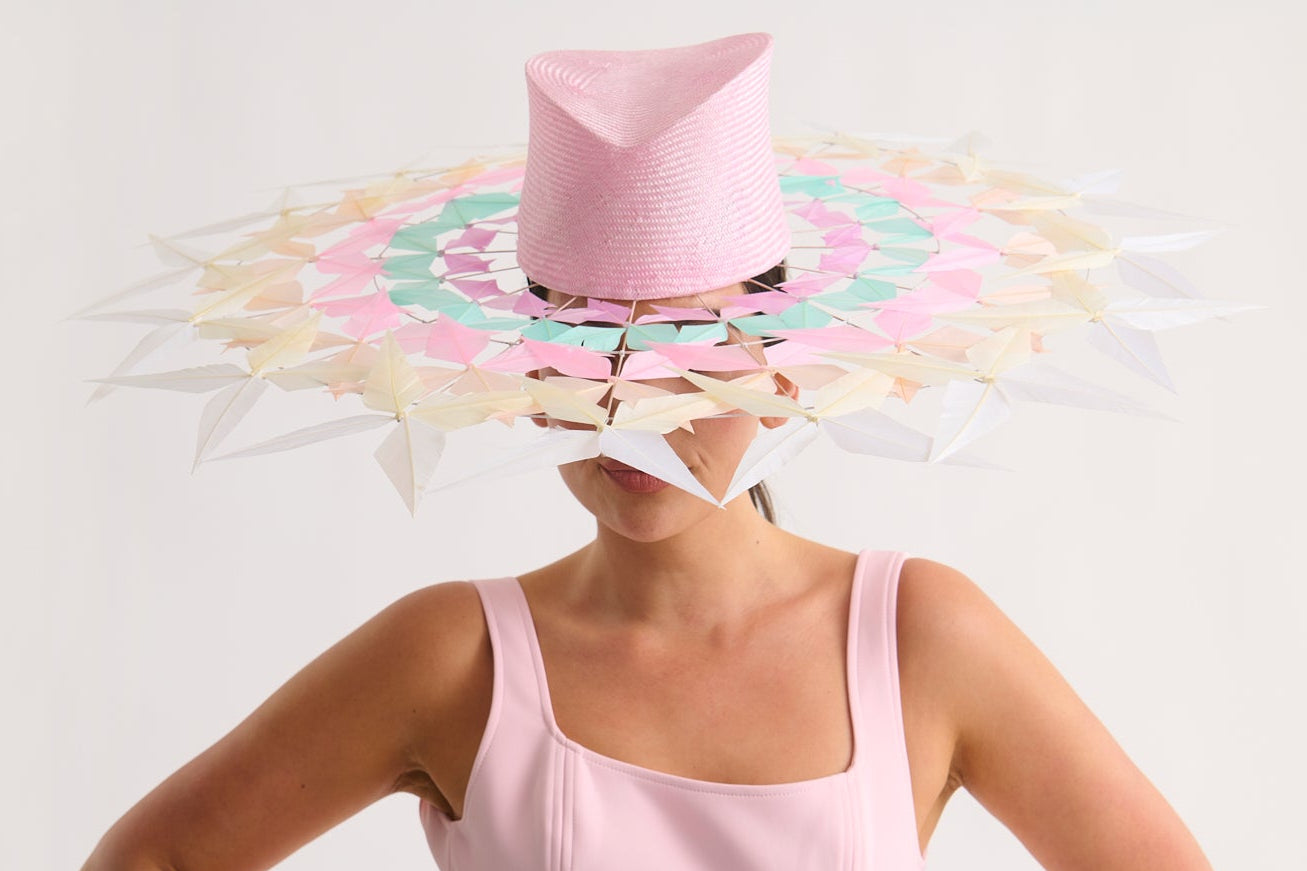 Woman wearing a wide feather brim hat and a pink dress against a white background