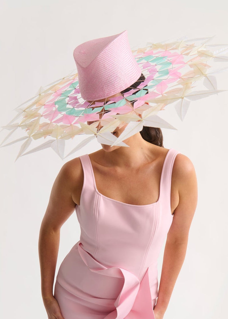 Woman wearing a wide feather brim hat and a pink dress against a white background